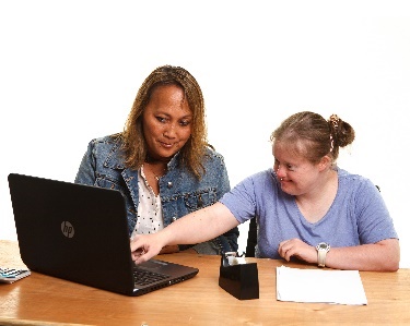 A woman helping a student with down syndrome use a laptop. 
