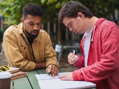 A man supporting a student with down syndrome to do their work.