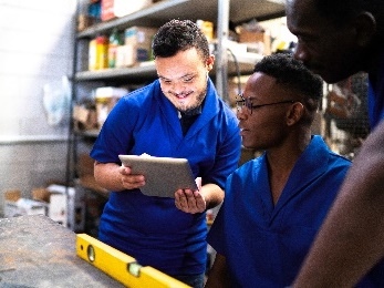 A group of people working in a warehouse. 2 of them are looking at a tablet together.